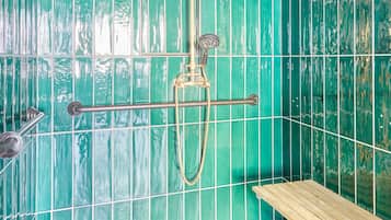 A shower with a handheld showerhead and a handheld faucet, a wooden shelf, and a metal shower seat.