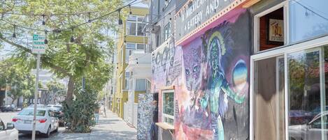 Une vue de rue avec une fresque sur un bâtiment, un panneau indiquant une zone de stationnement limitée à 30 minutes, et des voitures garées.