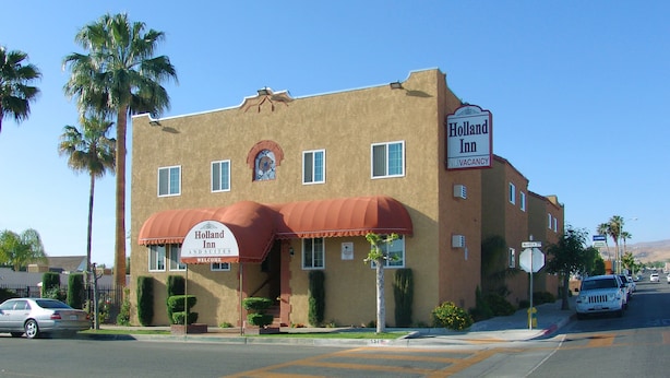 Un edificio de dos pisos con un toldo rojo y un letrero que indica 'Holland Inn and Suites', con un cartel de 'Habitaciones disponibles'.