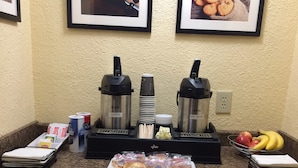 Una barra de desayuno con máquinas de café, una bandeja de pasteles y un cuenco de fruta.