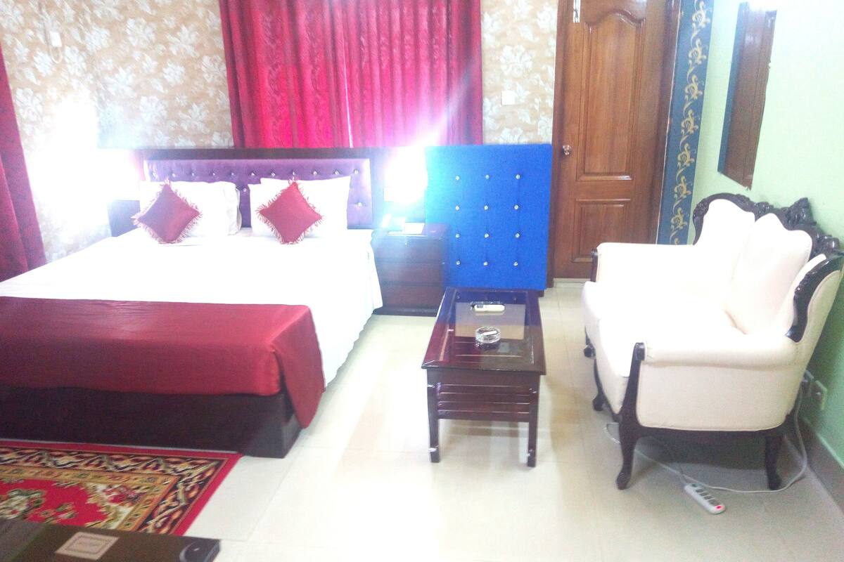 A hotel room with a bed, a nightstand, a blue upholstered chair, and a small table.