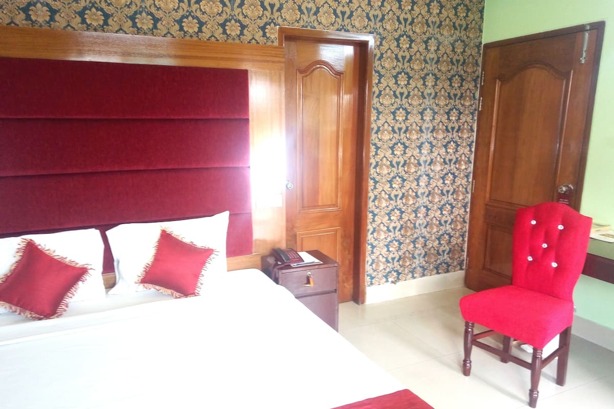 A room with a bed, a red chair, a wooden door, and a patterned wallpaper.