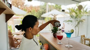 A person pouring a drink into a glass at an outdoor bar area with a wooden counter, a potted plant, and a cocktail with a lime garnish. - Chez Moi Suite and Spa (Siem Reap)