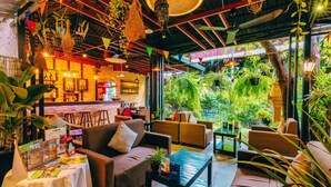 A cozy indoor seating area with sofas and tables, surrounded by lush greenery and hanging plants.