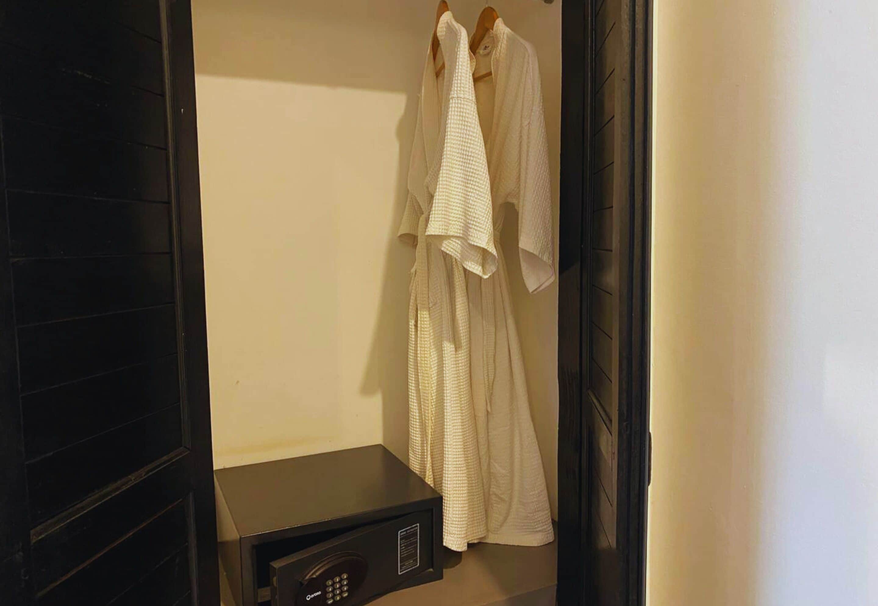 A room with a black cabinet, a white robe hanging on a wooden hanger, and a white towel on the floor.
