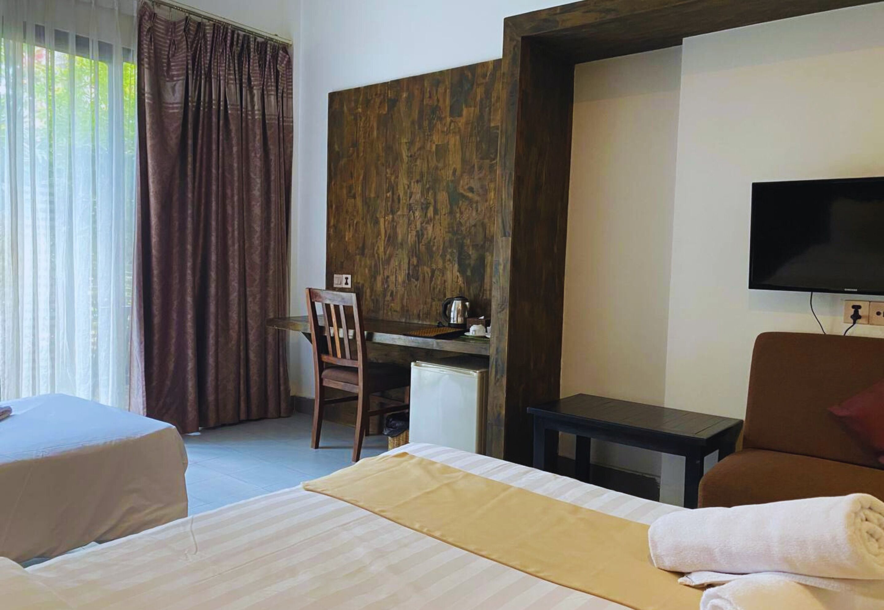 Habitación de hotel con cama, escritorio, silla, televisión y vistas al exterior.
