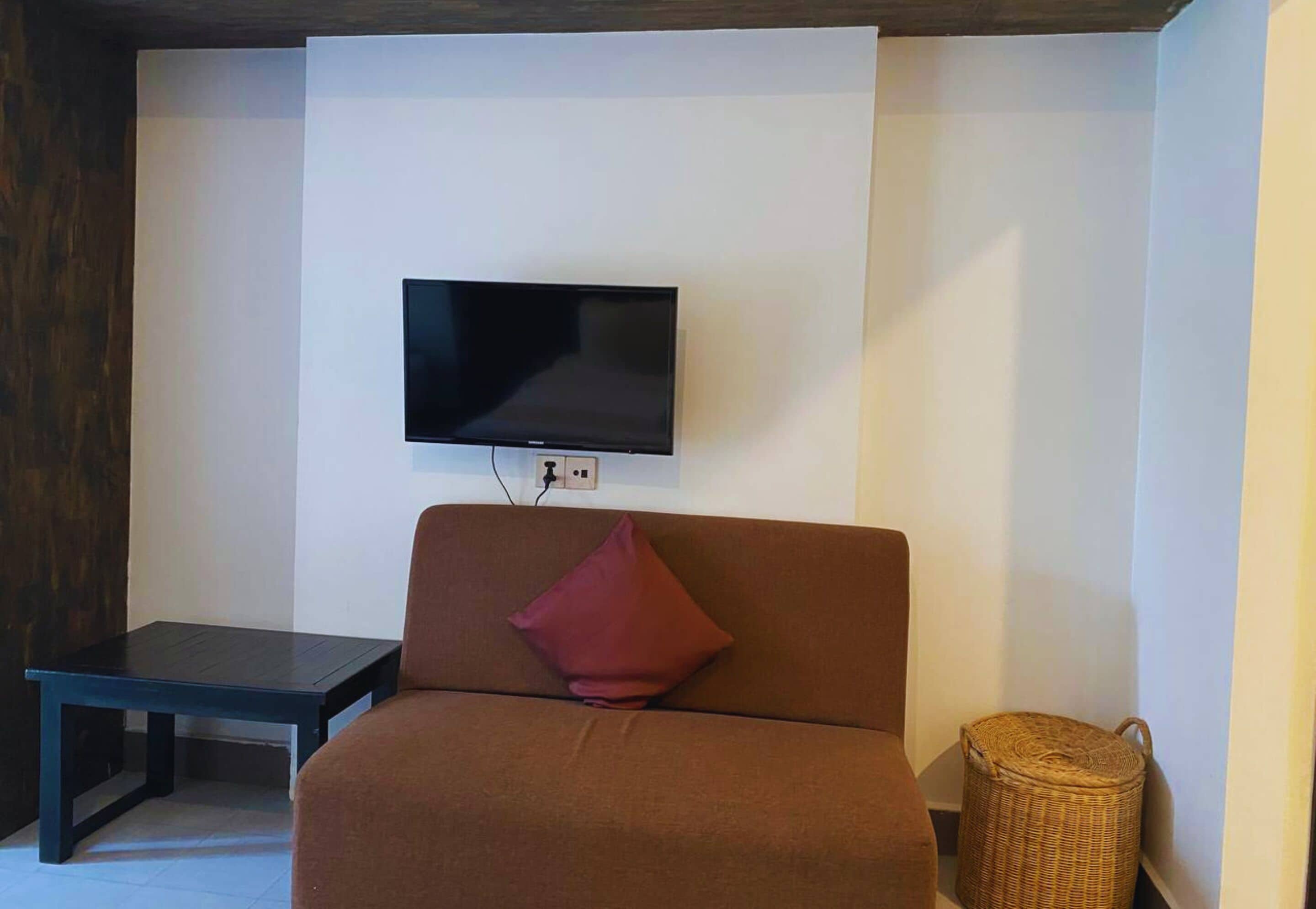 Un salon avec un canapé marron, une petite table, un téléviseur fixé au mur et un panier en osier.