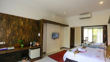 A hotel room with a wooden accent wall, a desk with a computer, a small fridge, a TV, two beds, and a window with curtains.