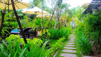 A garden pathway with lush greenery and outdoor seating areas with umbrellas.