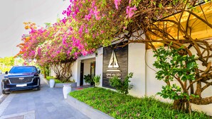 A modern building with a black awning, a blue SUV parked in front, and a well-maintained garden with pink flowers.