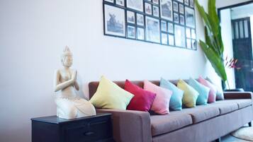 A statue on a nightstand, a sofa with colorful cushions, and a wall with framed pictures.