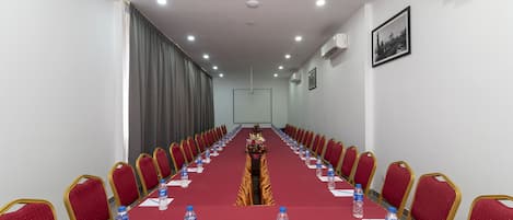A conference room with a long table, red chairs, water bottles, and a projector screen.