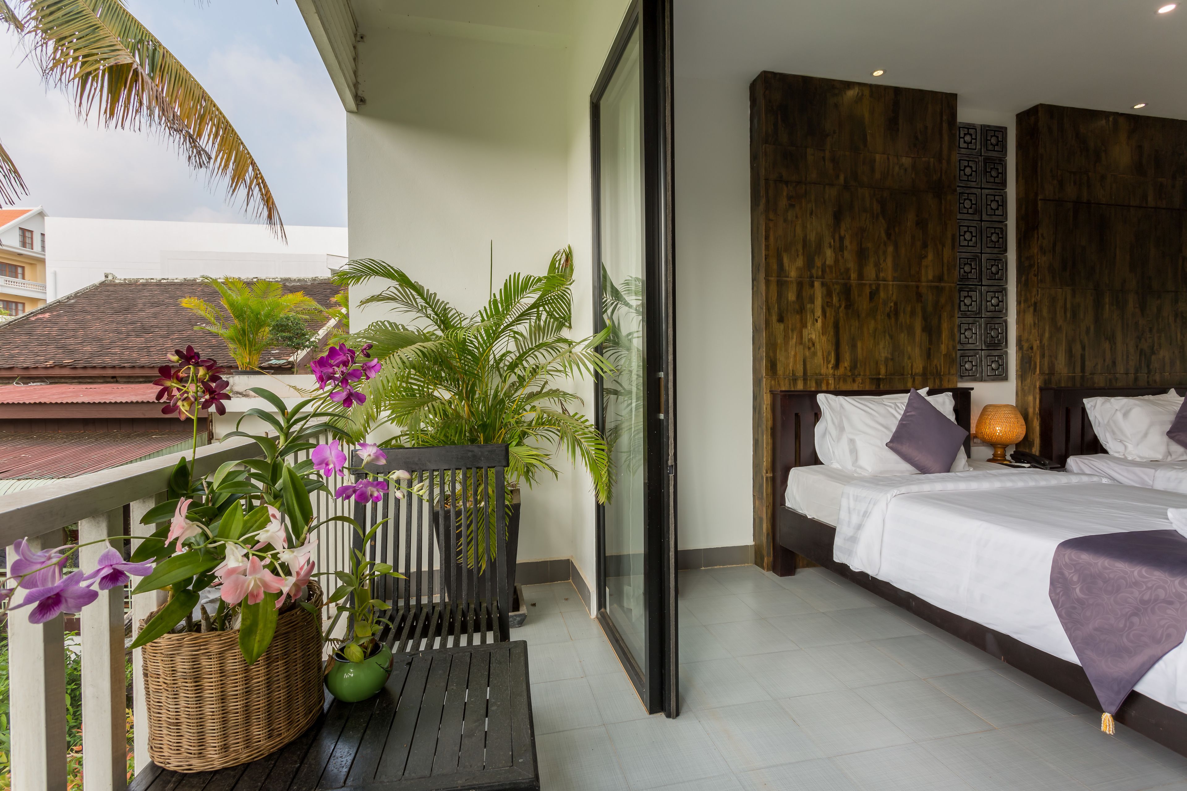 A balcony with potted plants and a bench, a bedroom with a bed and nightstand, and a view of the cityscape.