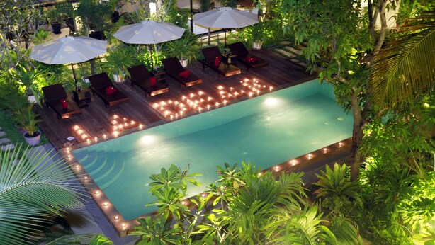 An outdoor swimming pool with lounge chairs and umbrellas, surrounded by lush greenery.