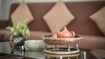 A table with a teapot and a bowl on a glass surface, a potted plant, and a brown sofa with diamond-shaped cushions in the background.