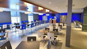 A modern dining area with multiple tables and chairs, large windows, and a blue accent wall. - Holiday Inn Express & Suites Vaudreuil by IHG (Vaudreuil)
