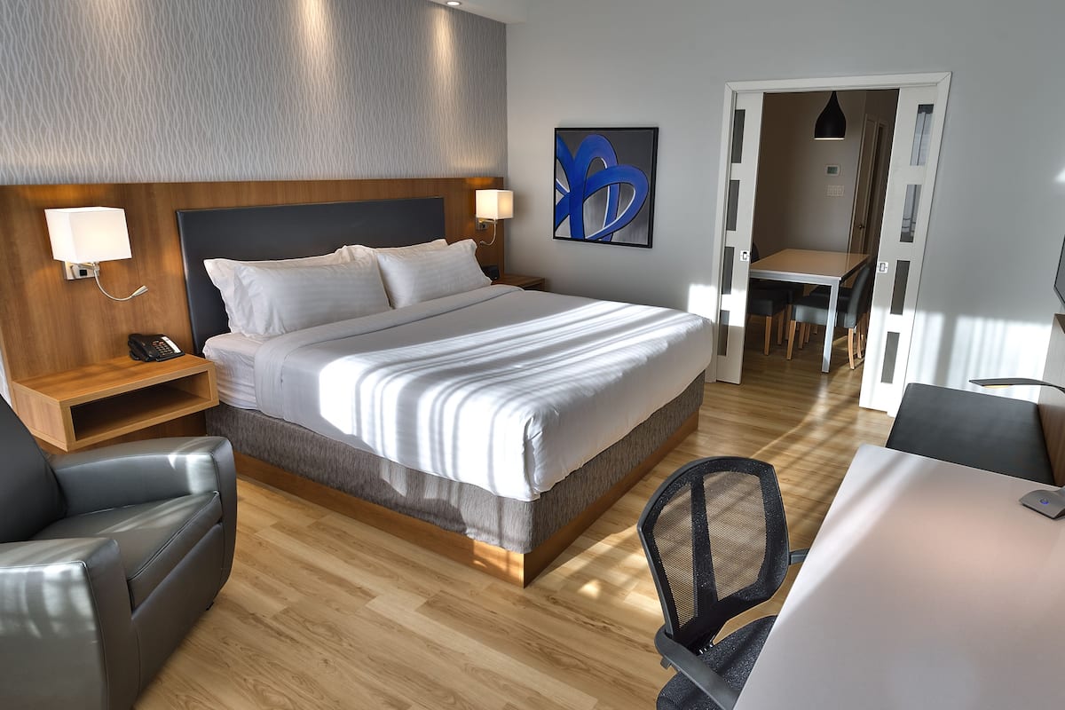 A hotel room with a bed, bedside lamps, a desk with a chair, a dining area, and a TV.