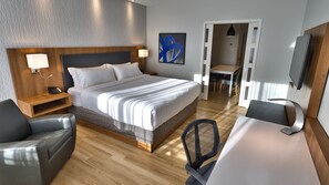 Une chambre d’hôtel comprenant un lit, des lampes de chevet, un bureau avec une chaise, un coin repas et un téléviseur.