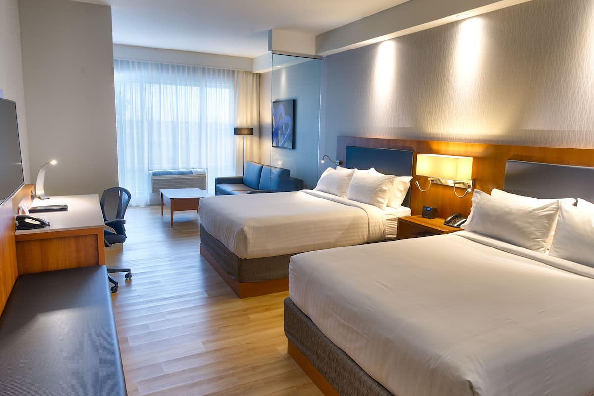 A hotel room with two beds, a desk with a computer, a chair, and a TV.