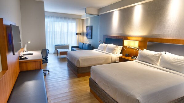 Une chambre d’hôtel avec deux lits, un bureau avec un ordinateur, une chaise et une télévision.