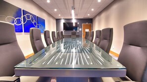 A conference room with a glass table and grey upholstered chairs.
