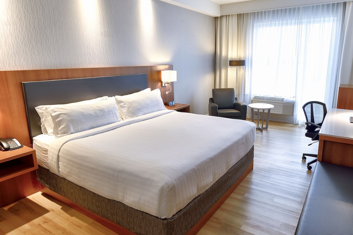 A hotel room with a large bed, a desk with a telephone, a chair, and a small table.