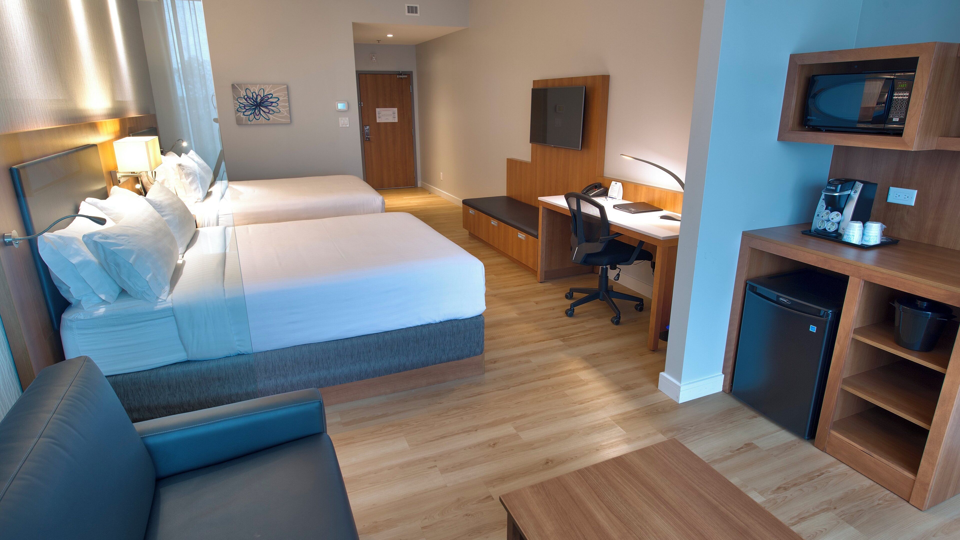 Habitación de hotel con dos camas, un escritorio, una silla, microondas, cafetera y refrigerador pequeño.