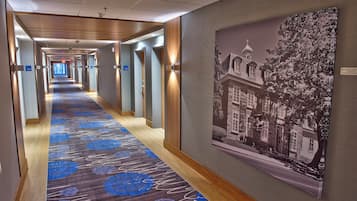 Un pasillo de hotel con alfombra estampada, puertas numeradas y un cuadro grande enmarcado en la pared.
