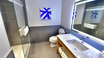 Une salle de bain moderne avec une douche à parois de verre, des toilettes blanches et un grand miroir au-dessus du lavabo.