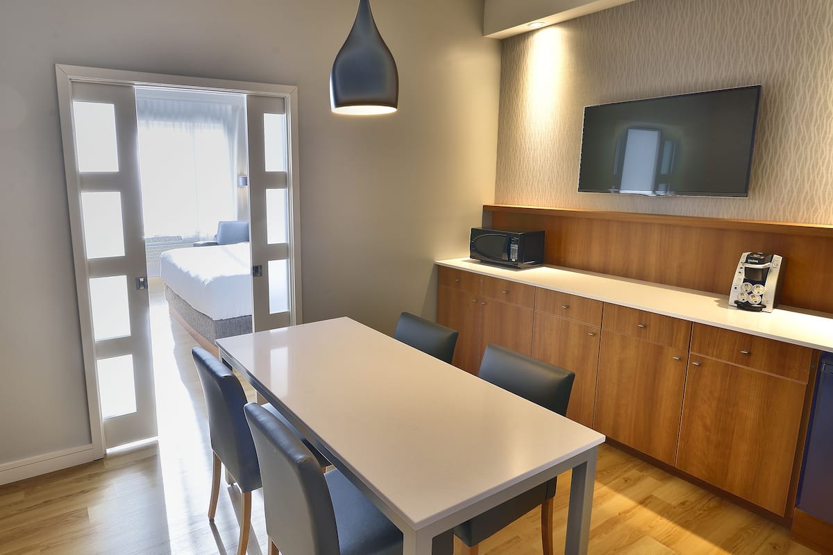 A modern kitchen with a dining area, wooden cabinets, a microwave, and a flat-screen TV.