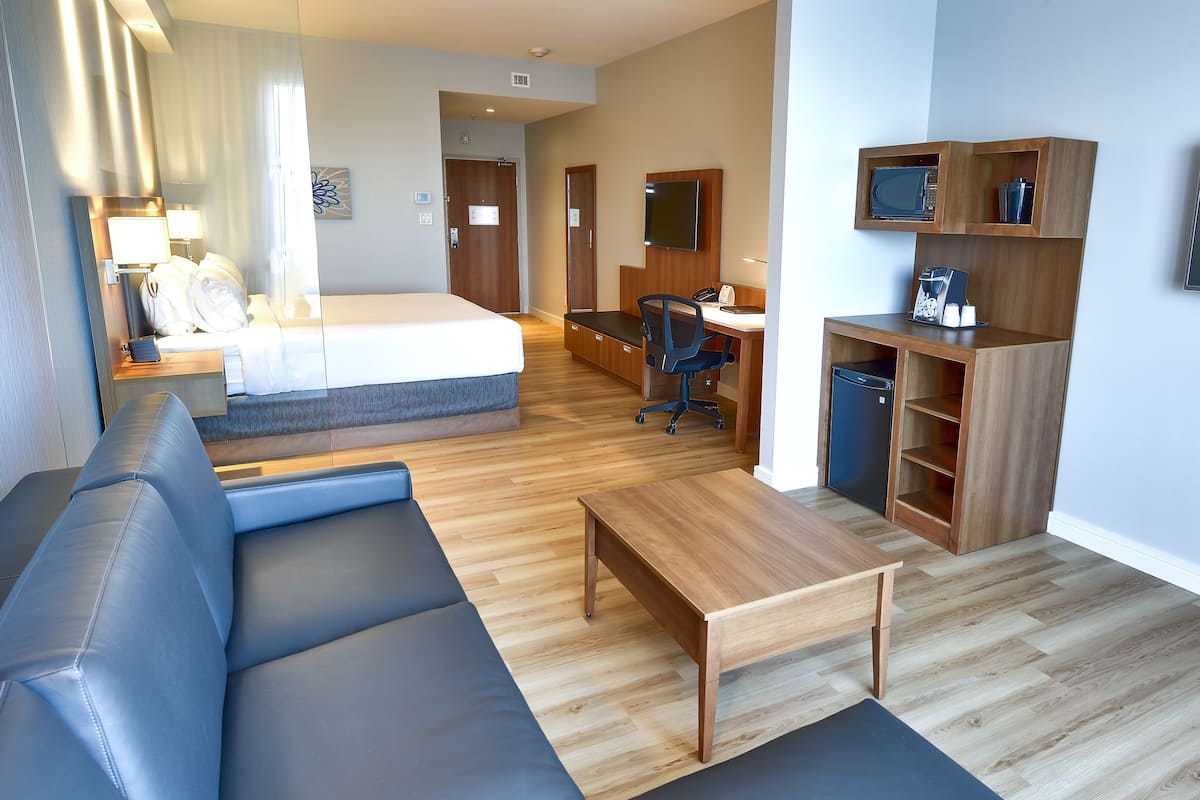 A modern hotel room with a bed, a sofa, a desk, and a TV.
