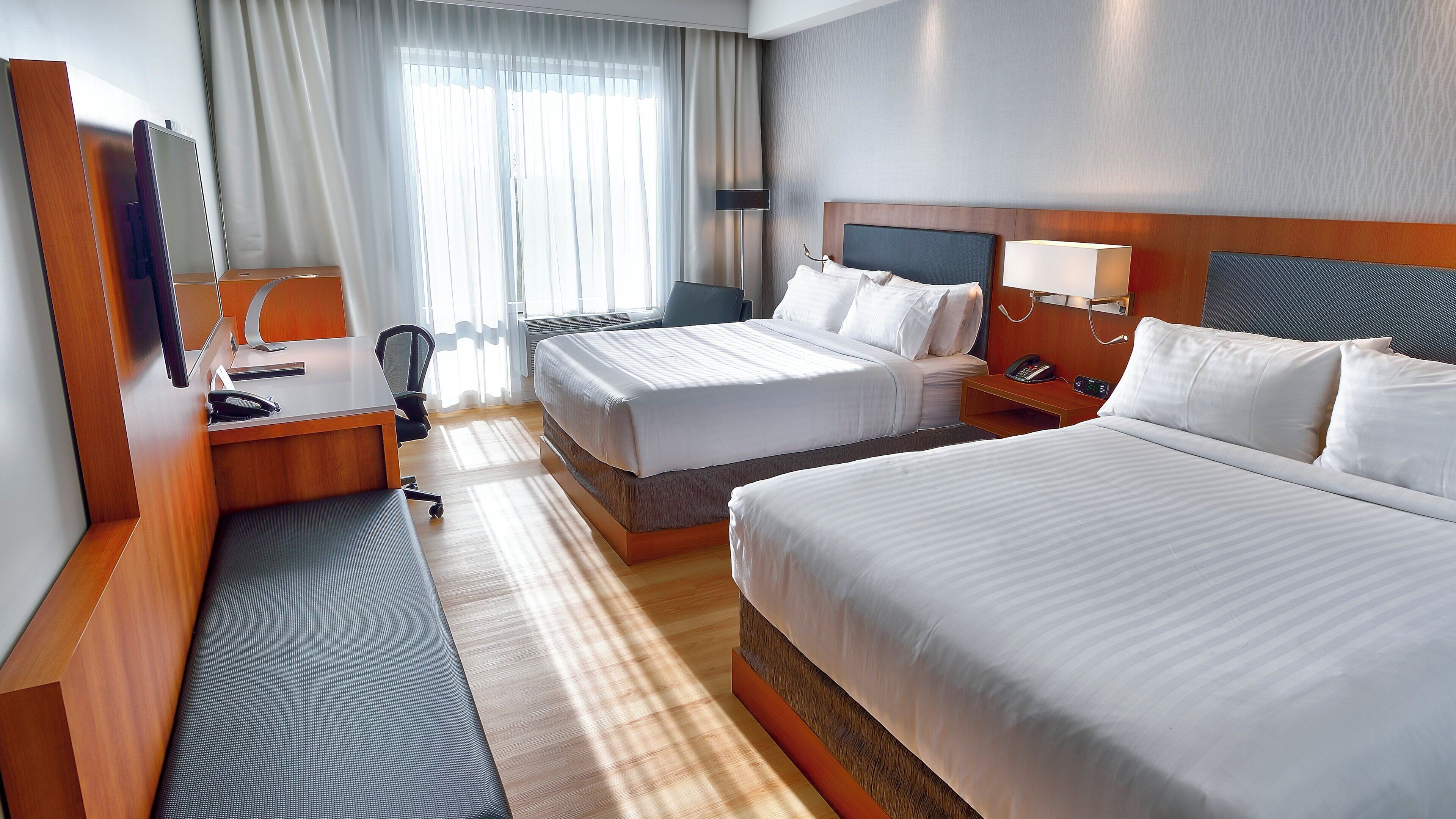 A hotel room with two beds, a desk, a chair, a telephone, and a lamp.