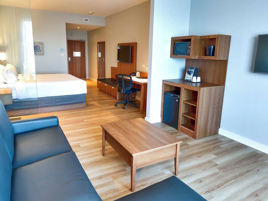 Ett modernt hotellrum med en säng, soffa, skrivbord och ett litet kök.