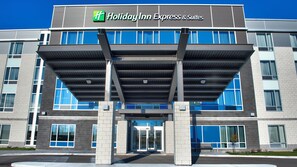 A Holiday Inn Express & Suites building with a covered entrance, large windows, and a clear sky.