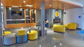 A modern lobby with a reception desk, seating area, and a TV screen.