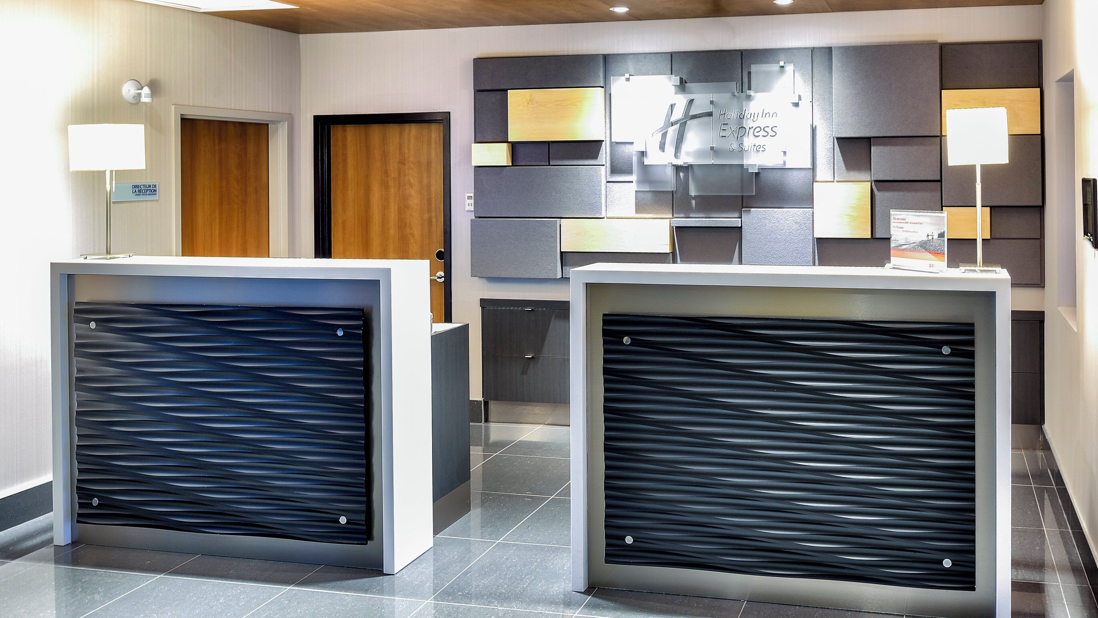 Ein Empfangsbereich im modernen Stil, mit einer Rezeption, einer Wandtafel für Holiday Inn Express & Suites und einer Stehlampe an der Rezeption.