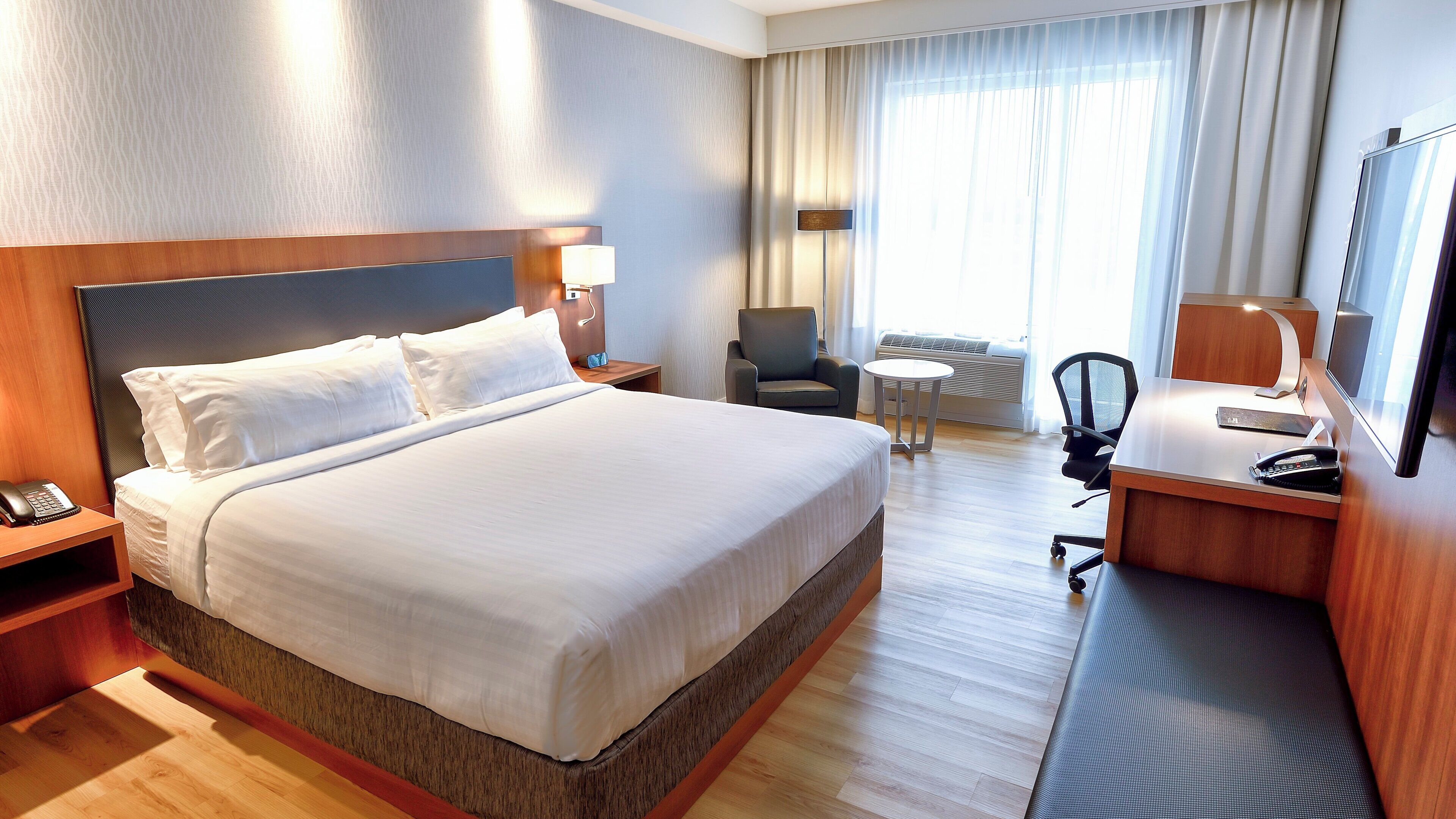 Habitación de hotel con una cama grande, un escritorio con teléfono, una silla y un televisor.