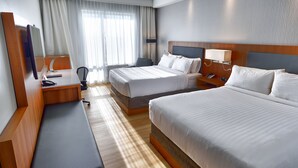 Une chambre d’hôtel avec deux lits, un bureau, une chaise, un téléphone et une lampe.