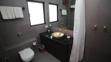 Un baño moderno con tocador negro, lavamanos dorado, inodoro blanco y un espejo grande.