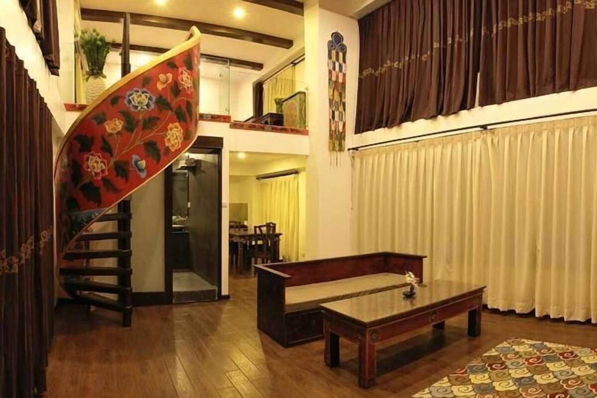 Un vaste espace de vie doté d’un plancher en bois, d’un escalier orné de motifs floraux, d’un coin repas et d’une grande fenêtre avec des rideaux.