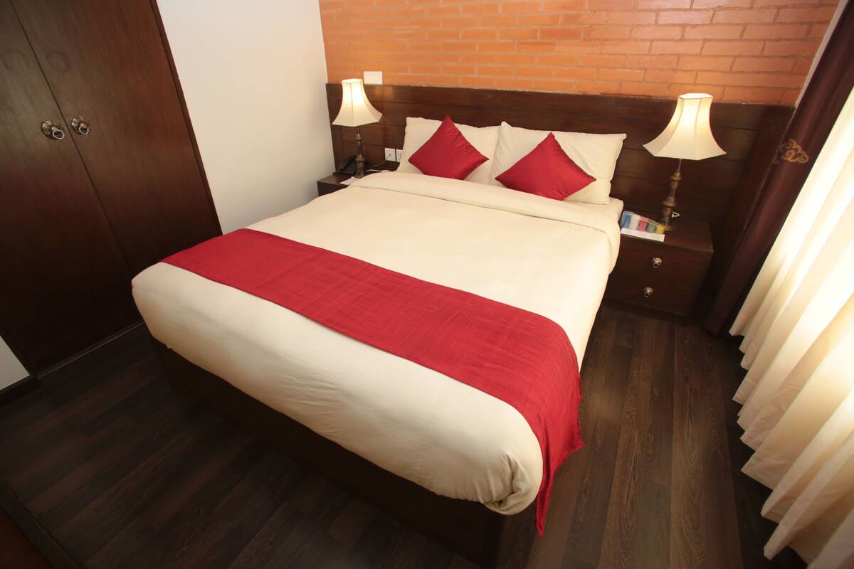 Une chambre d’hôtel avec un lit en bois, une literie rouge et blanche, une table de chevet avec une lampe et un mur en briques.