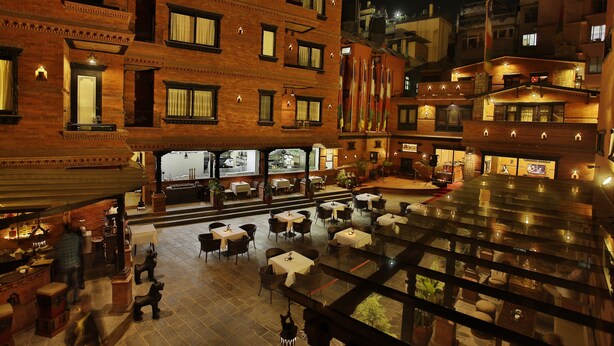 Hotel con patio que ofrece asientos al aire libre, un atrium de vidrio y varios pisos con balcones.