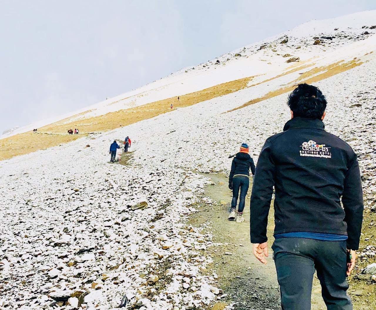 Una persona caminando por un sendero pedregoso, con otras personas al fondo.