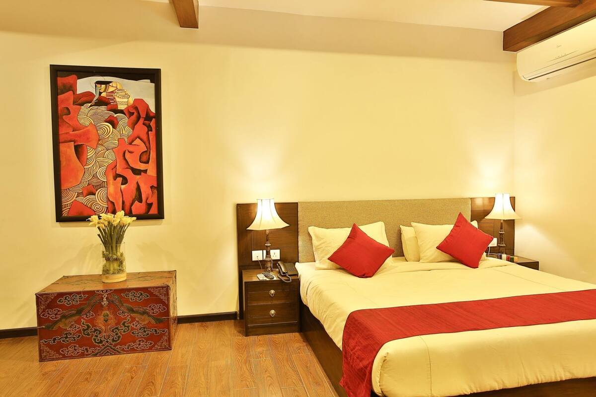 Une chambre d’hôtel avec un lit, des tables de chevet, une lampe, un vase avec des fleurs et un tableau au mur.