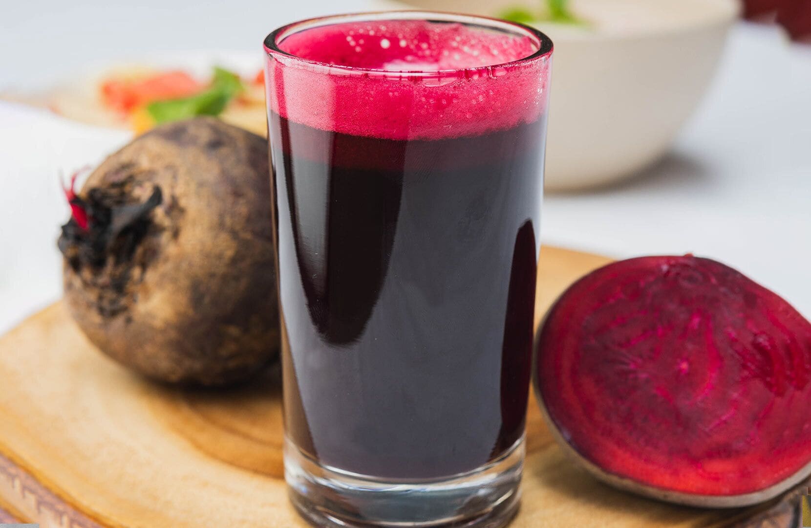 A glass of beetroot juice with a beetroot cut in half beside it.
