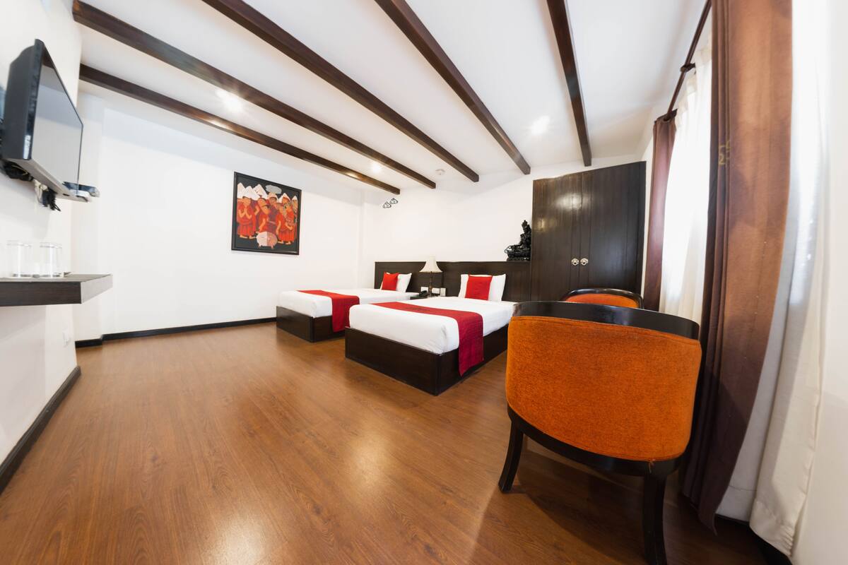 Une chambre d’hôtel avec deux lits, une chaise, un téléviseur et un tableau au mur.