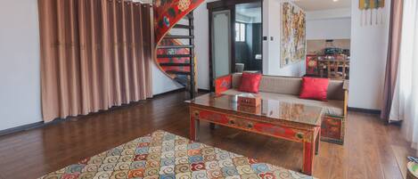Un salon spacieux agrémenté d’un grand tapis à motifs, d’une table basse en bois et d’un escalier en colimaçon.