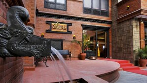 Entrada de un hotel boutique con una fuente tradicional, un banco y una planta en maceta.
