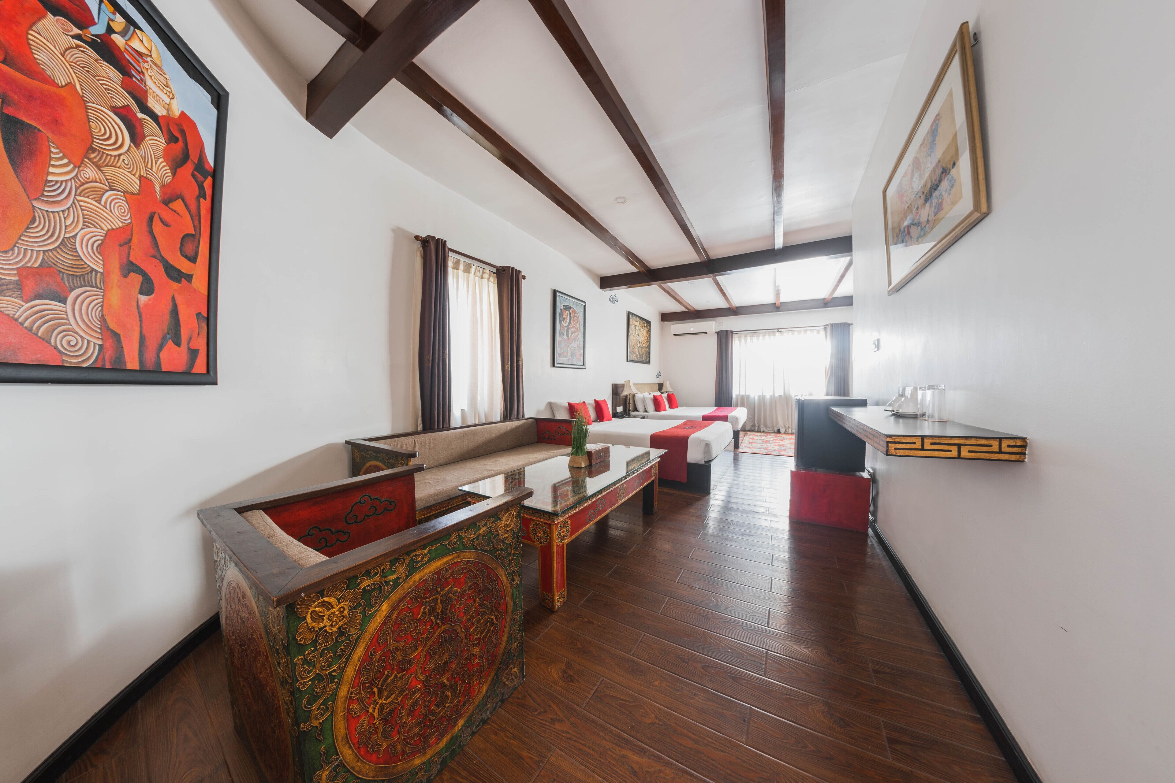 A spacious living room with a wooden floor, a sofa, a coffee table, and a decorative cabinet. There is a painting on the wall and a framed picture above the sofa.