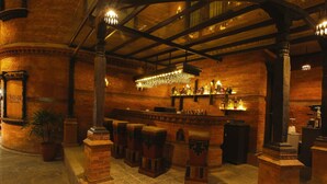 Zona de bar con paredes de ladrillo, taburetes de madera y una barra con botellas.